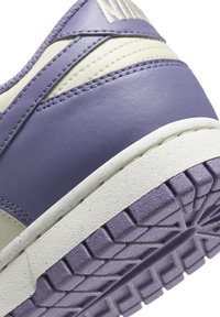 Purple synthetic sneaker showing a textured sole, cream accents, and detailed stitching. Features a rounded shape and distinctive tread pattern.