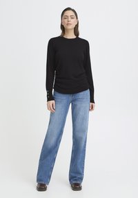 Czarna koszula z długim rękawem, okrągłym dekoltem i detalem z guzikami przy mankietach, w połączeniu z niebieskimi, szerokimi spodniami i brązowym obuwiem.