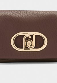Portafoglio in pelle marrone con un logo in metallo dorato ben visibile. Superficie testurizzata con una forma rettangolare elegante e linee pulite.