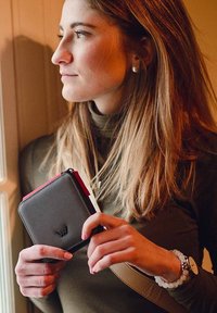 Compact black wallet with red zipper detail, featuring textured leather, square shape, and subtle embossed logo, held by a person.