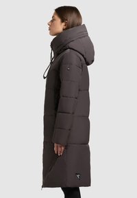 Czarny puchowy płaszcz w ciemnoszarym kolorze z wysokim kołnierzem, kapturem na sznurku i zamkiem błyskawicznym z boku. Posiada pikowane sekcje i akcent logo na końcu.
