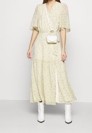 Abito maxi giallo floreale con maniche a sbuffo corte, scollatura a V e uno spacco laterale. Abbinato a una piccola borsa bianca e stivali bianchi.