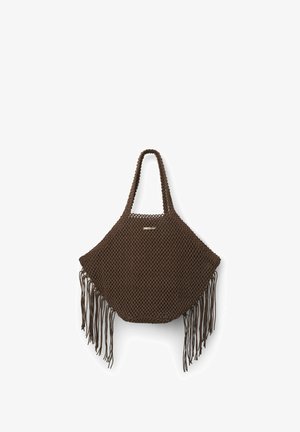 Sac cabas marron tricoté avec de longues anses et des franges suspendues aux coins inférieurs sur fond blanc.