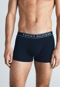 Marineblå boxershorts laget av elastisk stoff, med en kontrastkant i midjen med "TOMMY HILFIGER"-logoen i hvitt. Enkel, tettsittende design.