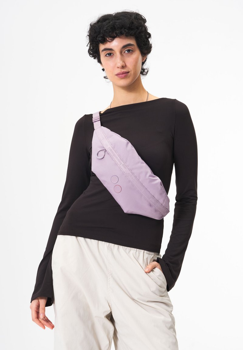 Lila Umhängetasche aus weichem Stoff, mit einem geschwungenen Design, verstellbarem Tragegurt und runden Akzenten in Rot und Blau.