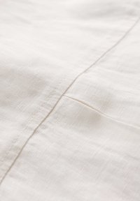 Tessuto di lino naturale di colore crema chiaro con una superficie liscia, caratterizzato da un sottile dettaglio di cucitura lungo un bordo.