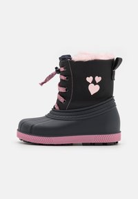 Botte imperméable noire avec accents roses, doublure en fausse fourrure, lacets roses et motifs de cœurs. Semelle texturée pour une meilleure adhérence. Design mi-mollet.