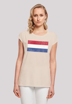 Beige T-Shirt mit einem lädierten grafischen Motiv der rot-weißen-blauen Flagge auf der Vorderseite. Kurzarm, runder Halsauschnitt, weicher Baumwollstoff.