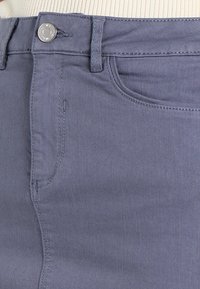 Pantalones de mezclilla ajustados en un tono azul claro, con un bolsillo frontal, lazos para cinturón y herrajes de botón en tono plateado. Textura suave con costuras sutiles.