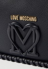 Černá texturovaná kabelka s tvarovaným černým srdcem a logem "M". Obsahuje zlaté branding "Love Moschino" a pletené černé lemování.