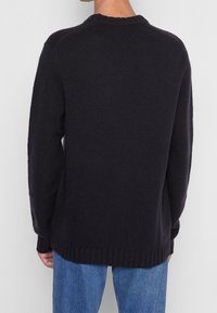 Dunkelblaues Strickpullover mit gerippten Bündchen und Saum, ausgestattet mit einem Rundhalsausschnitt und einer lockeren Passform. Das Material wirkt strukturiert und gemütlich.
