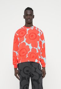 Κόκκινο φούτερ με λουλουδάτο μοτίβο σε ανοιχτό μπλε φόντο. Με ριμπ γιακά και μανσέτες, χαλαρή εφαρμογή. Συνδυασμένο με σκούρο γκρι παντελόνι με μοτίβο.