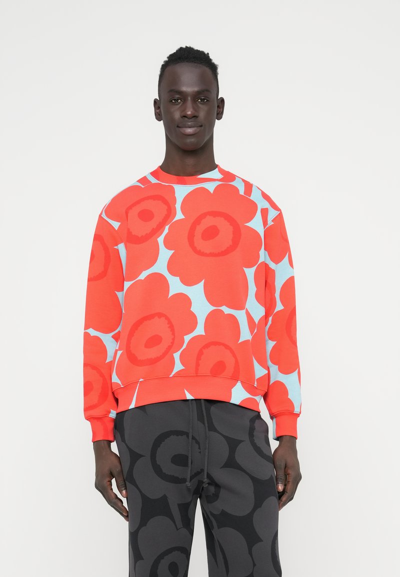 Κόκκινο φούτερ με λουλουδάτο μοτίβο σε ανοιχτό μπλε φόντο. Με ριμπ γιακά και μανσέτες, χαλαρή εφαρμογή. Συνδυασμένο με σκούρο γκρι παντελόνι με μοτίβο.