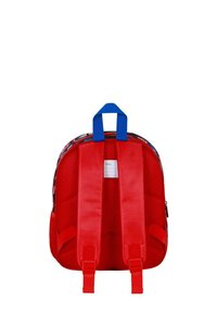 Sac à dos rouge avec une poignée bleue et des bretelles rembourrées. Présente une surface texturée et une section pour une étiquette au dos. Design compact.