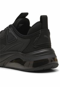 Zwarte sportieve schoen met een gestructureerde mesh bovenkant, vormgegeven accenten en een glanzend hielgedeelte. PUMA-logo aan de zijkant.
