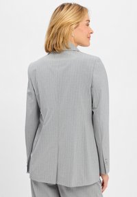 Szary żakiet w paski z dopasowanym krojem, z pojedynczym rozcięciem z tyłu i zapięciem na guziki przy mankietach. Gładka tekstura i elegancki design.
