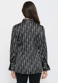 Camicia nera in satin con maniche lunghe, caratterizzata da un motivo a catena bianca e polsini con bottoni. Design del colletto classico con taglio dritto.