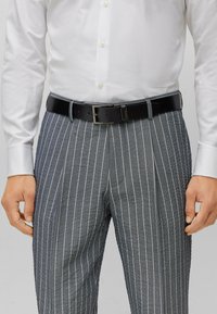 Black leather belt with a simple rectangular buckle, worn with gray striped trousers and a white dress shirt.