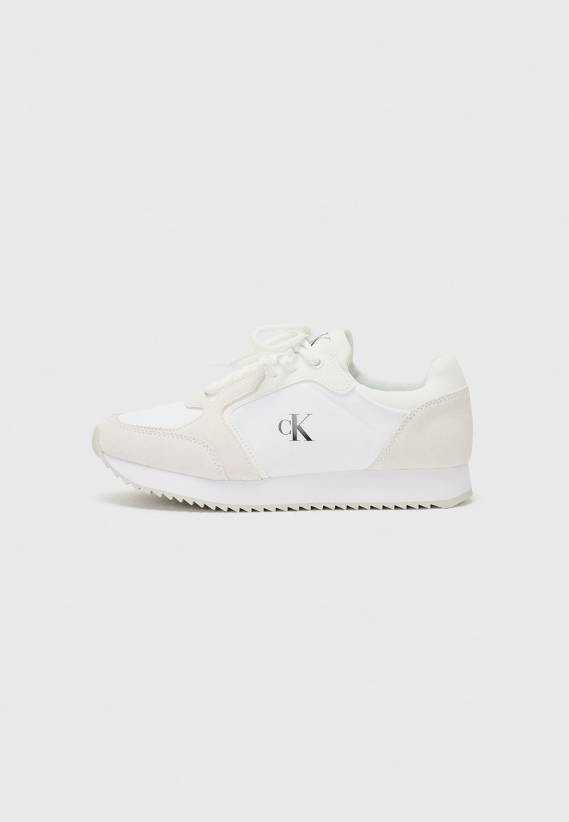 Hvit og beige atletisk sneakers med snøring, overdel i semsket skinn og stoff, rillestruktur på gummisåle og trykt logo på siden.