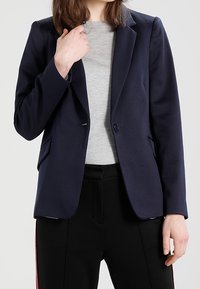 Navyblazer i slätt tyg, med en knappknäppning, två framfickor och en klassisk kragsdesign.