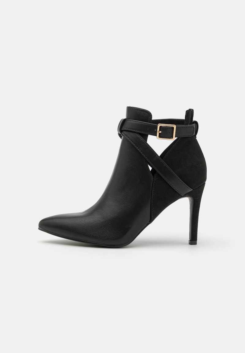 Bottine noire en cuir et daim, dotée d'une pointe effilée, d'un talon stiletto et d'une bride croisée avec une boucle dorée.