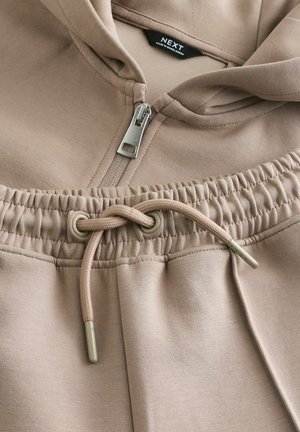 Light brown sweatshirt with a zipper and hood. Features a drawstring at the waist with plastic tips and smooth, soft texture.
