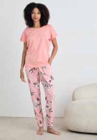 Ljusrosa bomullströja i kombination med pyjamasbyxor med blommönster i liknande rosa toner, med elastisk midja och dragsko.