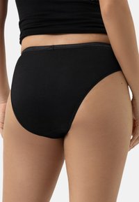 Slip nero in cotone con design a vita alta, texture liscia e un bordo semplice e senza cuciture lungo le aperture delle gambe e della vita.