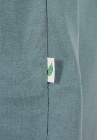 Grön bomullstyg med ribbad textur. Har en liten vit etikett med en grön lövdesign sydd på sömmen.