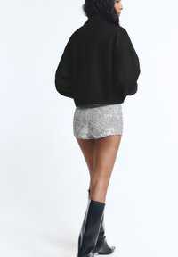 Veste noire courte, shorts en sequins argentés brillants et bottes noires montantes. Textures de tissu lisses, couleurs contrastées et coupe ample.