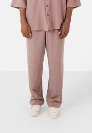 Conjunto de dos piezas holgado en suave tela beige. La parte superior tiene mangas cortas y botones; los pantalones son largos y con un corte relajado.