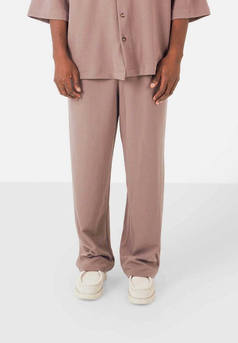 Lockere zwei-teilige Outfits aus weichem, beigem Stoff. Das Oberteil hat kurze Ärmel und Knöpfe; die Hose ist lang und hat eine entspannte Passform.