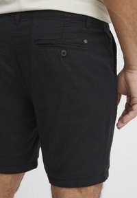 Sorte shorts med en knappet baklomme, rette ben og en myk tekstur, med synlig søm og en ren kant.