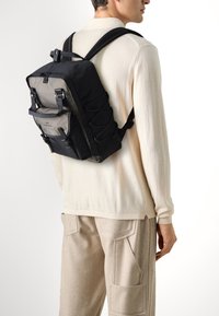 Sac à dos noir et gris avec des bretelles réglables, une poche avant et un design de cordon élastique. Fabriqué en tissu résistant avec une silhouette moderne et élégante.