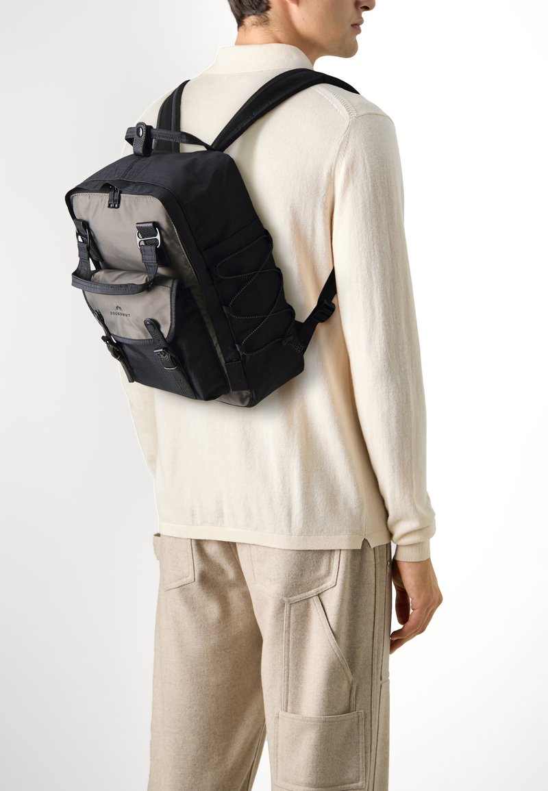 Sac à dos noir et gris avec des bretelles réglables, une poche avant et un design de cordon élastique. Fabriqué en tissu résistant avec une silhouette moderne et élégante.