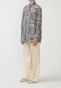 Camicia a righe bianco e nero con colletto a bottoni, dotata di maniche lunghe e vestibilità comoda, abbinata a pantaloni beige a gamba larga.