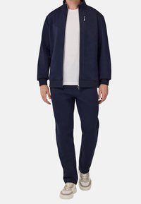 Navy blue tracksuit with a zip-up jacket and matching pants. Smooth fabric, ribbed cuffs, and a subtle design detail on the jacket.