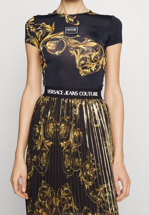 Top negro de manga corta con estampado dorado ornamentado, que presenta una etiqueta con el logotipo. Combinado con una falda negra de tablas adornada con acentos dorados.