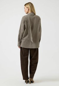 Brun ternet skjorte med lange ærmer og krave, kombineret med mørkebrune bukser. Glat stoftekstur, afslappet pasform, minimalistisk design.