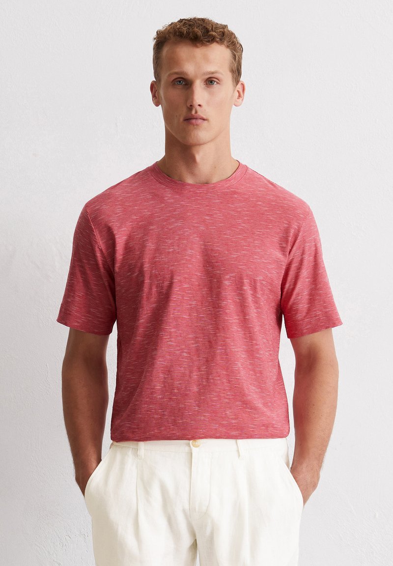 Czerwony t-shirt z krótkim rękawem o melanżowej fakturze i klasycznym okrągłym dekoltem, zestawiony z kremowymi lnianymi spodniami. Prosty, casualowy design.