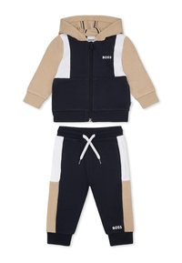 Ensemble de surv êtement zippé à capuche en bleu marine, beige et blanc. Tissu doux, avec un design coloré en blocs et un pantalon à cordon de serrage ajustable.