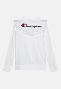 Bijela dukserica od pamuka. Ima kapuljaču s vezicom i vidljiv "Champion" logo na leđima u crnoj i crvenoj boji. Elastični manšeti i donji rub.