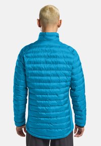 Giacca isolante blu con colletto alto, caratterizzata da un design trapuntato, una texture liscia e una parte posteriore più lunga.