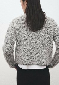 Teksturirani pleteni džemper u crno-bijeloj kombinaciji, kroja do struka, s spuštenim ramenima i mekim, toplim izgledom, slojevit preko bijele košulje.