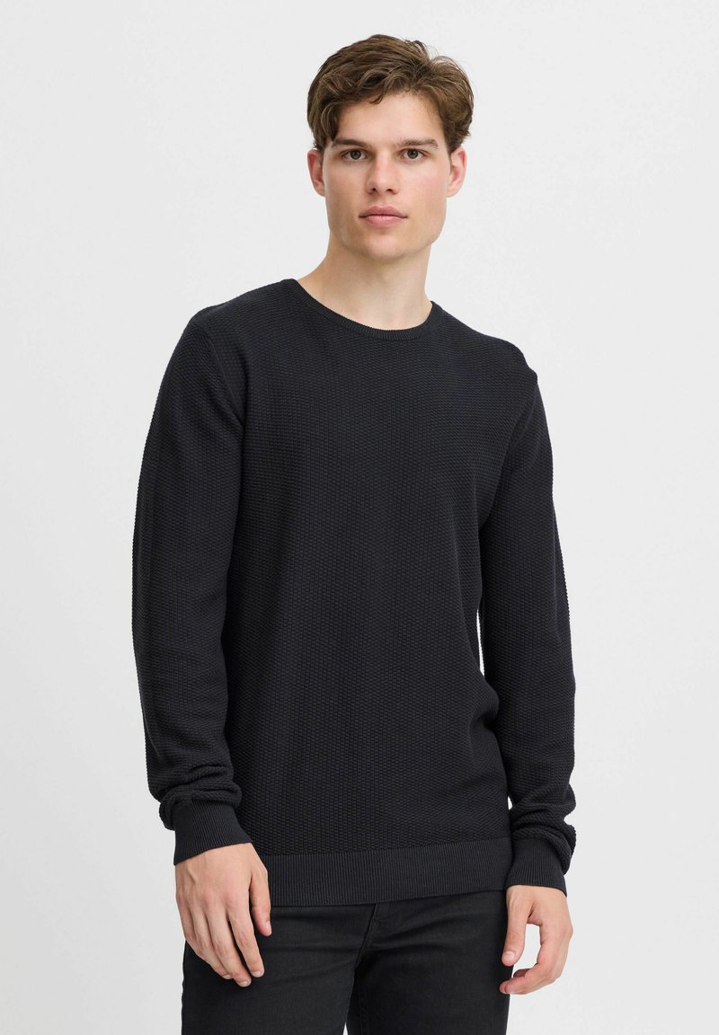 Pulover negru din tricot cu un model texturat, guler rotund și mâneci lungi. Manșetele și tivul ribbate oferă un aspect ajustat. Purtați-l cu pantaloni negri.
