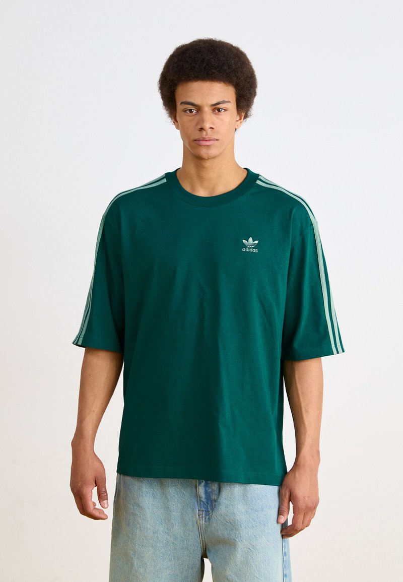 Grøn bomulds t-shirt med korte ærmer, der har tre hvide striber langs skuldrene og et lille logo på brystet.