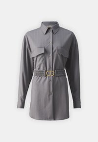 Chemise grise à boutons avec des rayures verticales, deux poches poitrine, des manches longues et une taille froncée avec une boucle dorée.