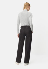 Graues Langarmshirt kombiniert mit hochtaillierter schwarzer Denim-Hose, mit einem geraden Bein und Gesäßtaschen, aus der Rückansicht dargestellt.