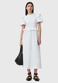 Witte mid-lange jurk met pofmouwen, gerimpelde buste, gerimpelde taille en een gladde textuur, gecombineerd met een zwarte tas en sandalen.