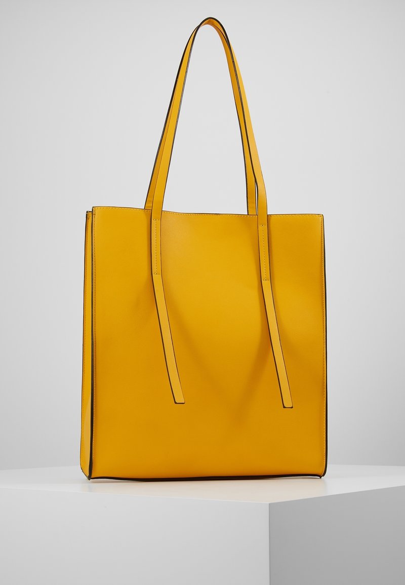 Borsa tote gialla in pelle liscia, con due manici lunghi e cuciture nere a contrasto lungo i bordi. Design minimalista.